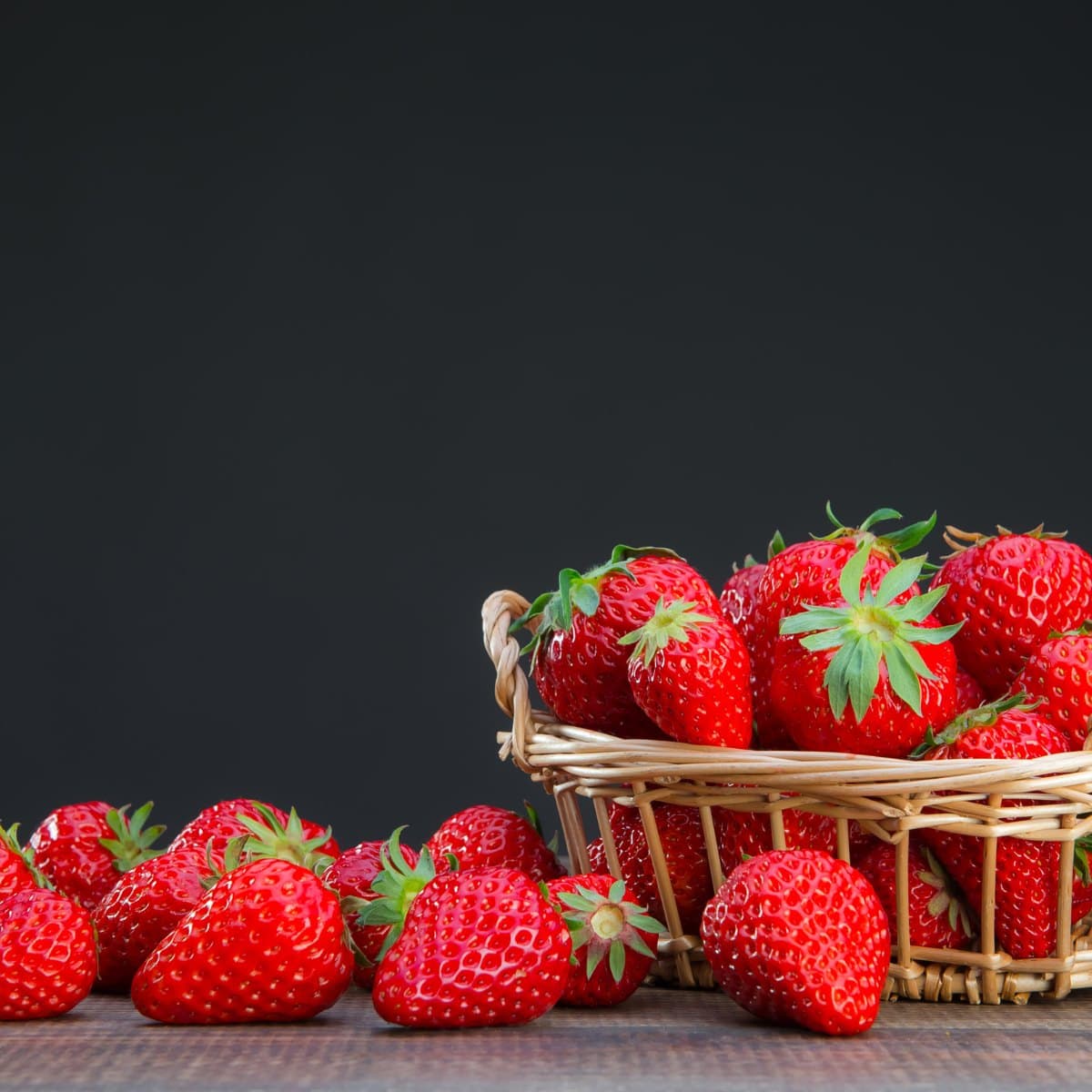 A basket of strawberries against a dark ground