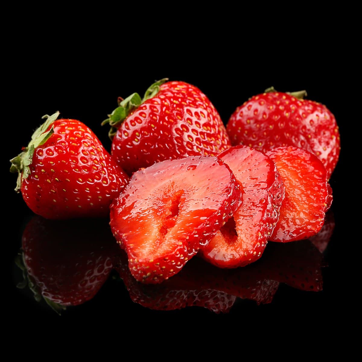 Whole strawberries and cut halves on a dark reflective surface